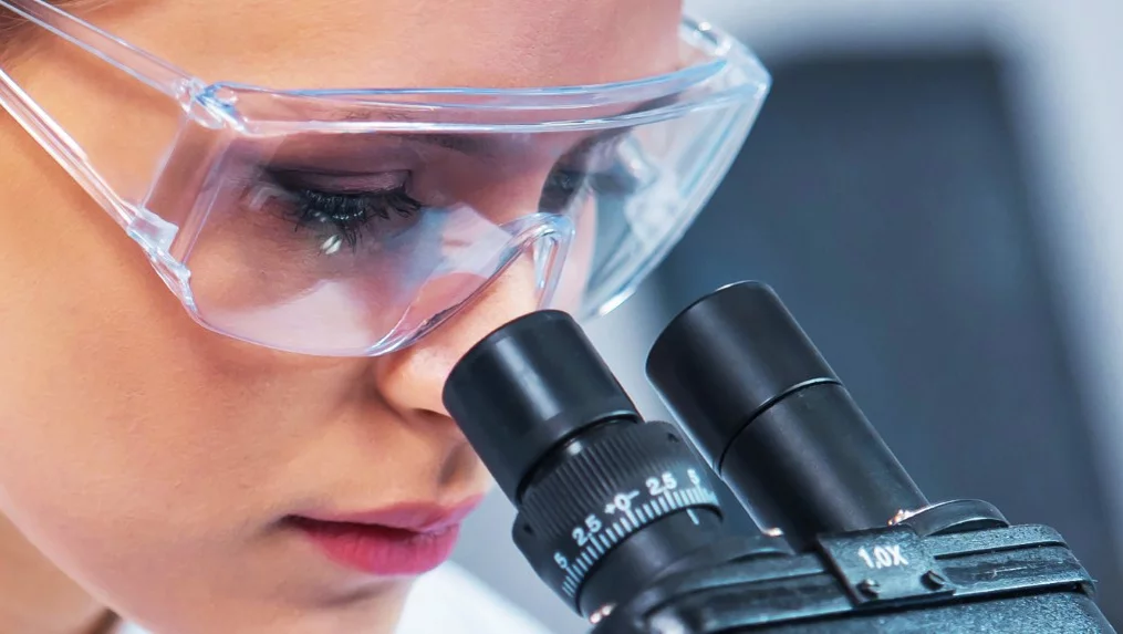 Nahaufnahme einer Wissenschaftlerin, die in ein Mikroskop schaut.